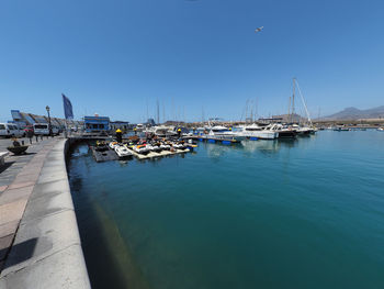 Sailboats moored in harbor against clear blue sky