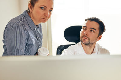 Business people discussing data on computer screen. woman talking to young male coworker in office