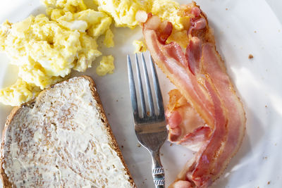 Overhead view of eggs, bacon, and toast on white plate with fork