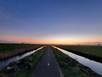 Empty road amidst field against sky during sunset