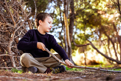 Full length of boy sitting by tree against plants