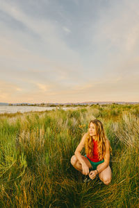 Young woman sitting on grass in field against sky