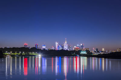 Illuminated buildings by river against sky at night