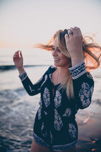 Full length of smiling young woman standing against sky