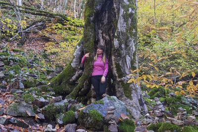 Portrait of woman standing by tree trunk in forest