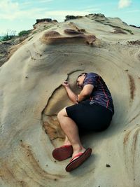 Midsection of man sitting on rock at beach