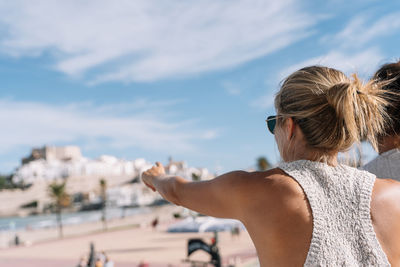 Rear view of woman wearing sunglasses against sky in city