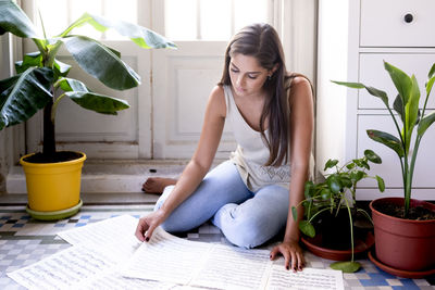 Young woman sitting on potted plant at home