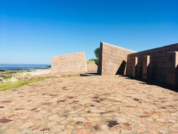 Walkway leading towards sea against clear blue sky