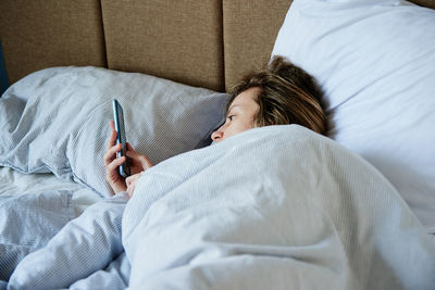 Woman using smartphone in the bed, social media, lazy weekend