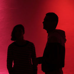 Silhouette man and woman standing against red wall during sunset