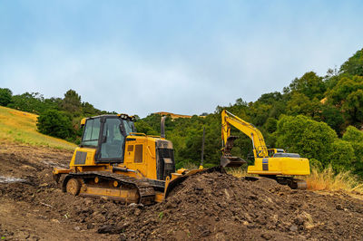 View of yellow bulldozer and excavator on plot of land. heavy equipment clears area. 