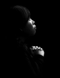 Woman looking up with hands clasped against black background