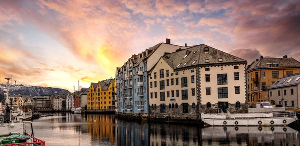 Sailboats moored on canal by buildings against sky during sunset