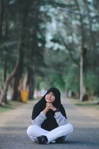 Young woman wearing hijab sitting on road