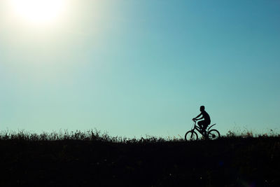 Silhouette of person on bike against clear sky