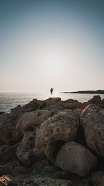 Man standing on rocks by sea against clear sky