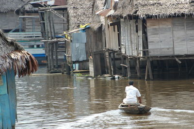 Rear view of man sitting in canal against building