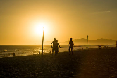 Silhouette people on beach against sky during sunset