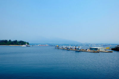 Boats moored at harbor against clear blue sky