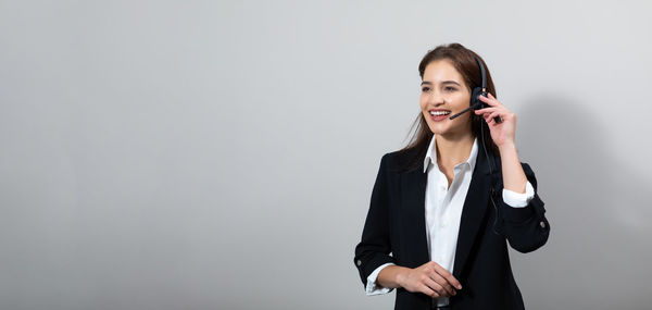 Young woman using phone while standing against white background