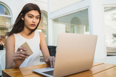 Young woman looking through smart phone while sitting on table