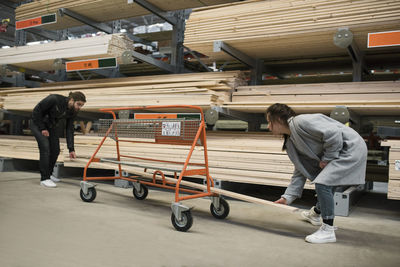 Couple placing wooden plank in trolley at hardware store