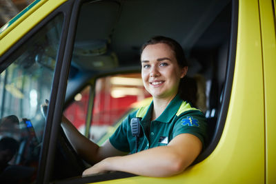 Portrait of smiling young female paramedic driving ambulance in parking lot