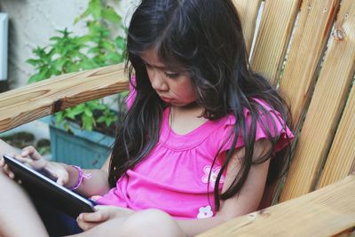 High angle view of girl using digital tablet on chair in back yard