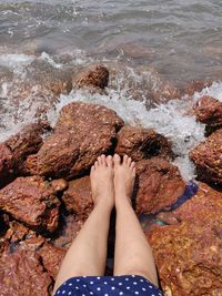 Low section of man relaxing on rock at beach