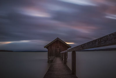 Wooden pier on sea against cloudy sky during sunset