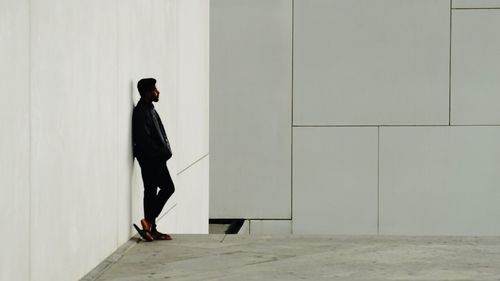 Side view of man walking on footpath against wall