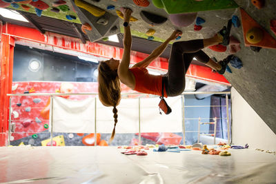 Side view of strong female athlete in sportswear clambering wall in modern bouldering center