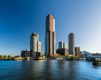 Modern buildings by river against blue sky