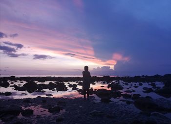 Silhouette people standing on rock at beach against sky during sunset