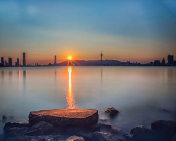 Scenic view of sea by buildings against sky during sunset