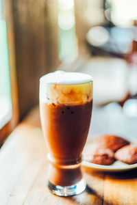 Iced cocoa drink with whipped cream and brownie cookies on wood table.