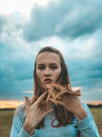 Portrait of young woman standing against cloudy sky