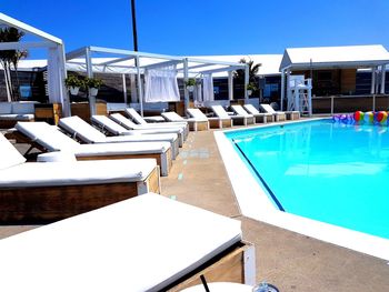 Empty chairs by swimming pool against clear blue sky