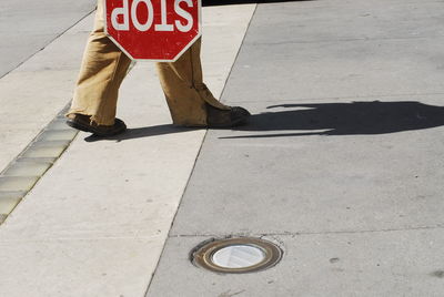 Low section of person walking with stop sign on sidewalk