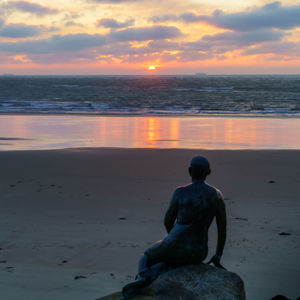 Rear view of rock on beach against sky during sunset