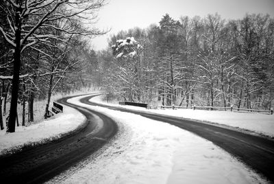 Snow covered road amidst trees during winter