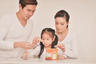 Parents teaching savings to daughter against white background