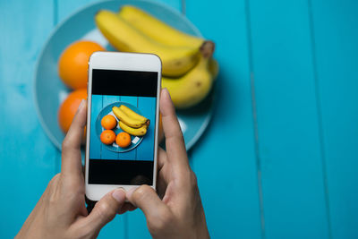 Cropped hands of woman photographing fruits in plate on wooden table