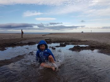 Boy playing on beach against sky during sunset