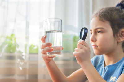 Side view of girl looking at water through magnifying glass at home