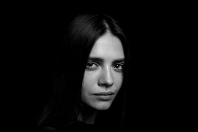 Close-up portrait of smiling young woman over black background