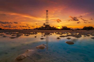 Reflection of rocks in sea against sky during sunset