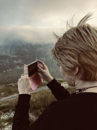 Woman photographing with mobile phone against sky