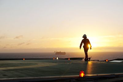 Man standing on sea against sky during sunset